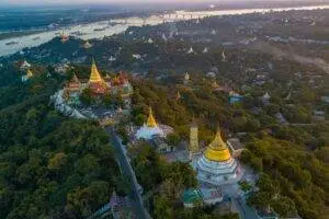 Breathtaking aerial view of Mandalay Hill with its golden temples at sunrise, overlooking the Irrawaddy River.