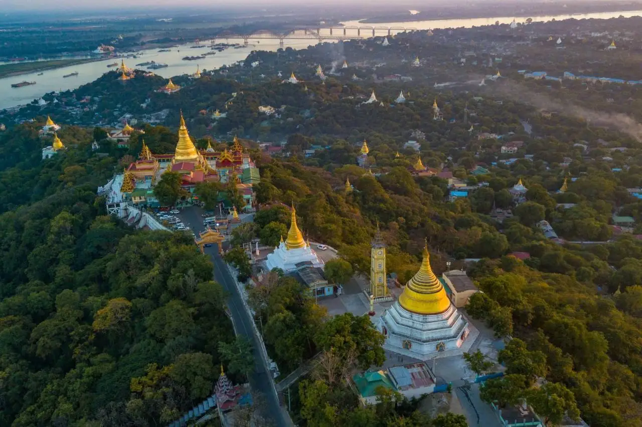 Breathtaking aerial view of Mandalay Hill with its golden temples at sunrise, overlooking the Irrawaddy River.