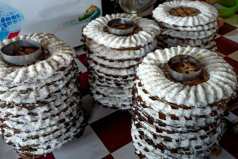 From above of white noodle placed on wooden caps and drying on tile floor in manufacture in light place