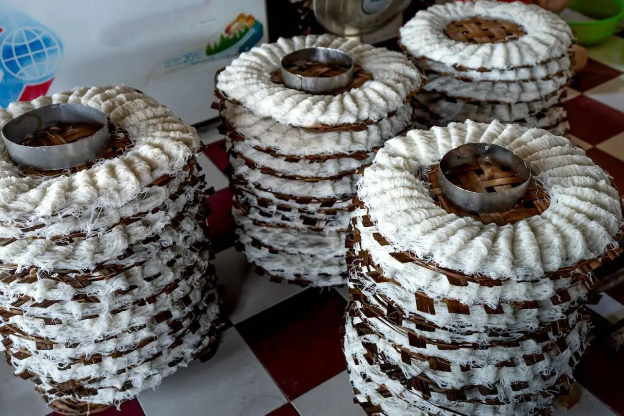 From above of white noodle placed on wooden caps and drying on tile floor in manufacture in light place