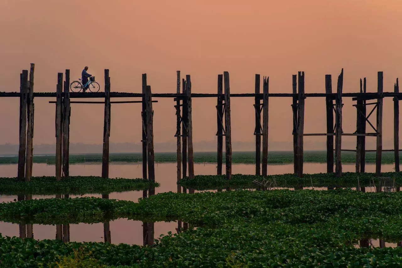 Cyclist silhouetted against the sunset on U Bein Bridge in Mandalay representing the best time to visit Amarapura in 2026